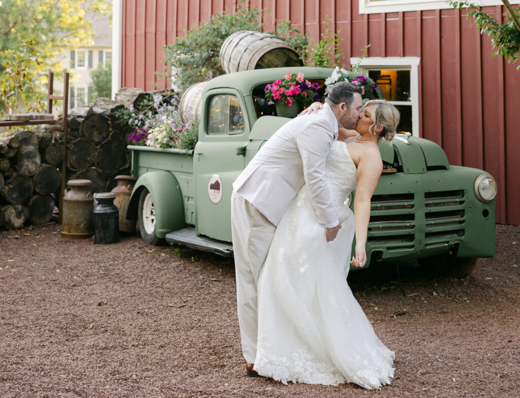Bride and groom kissing in front of green truck at barn venue Lochwood Manor in Skippack PA
