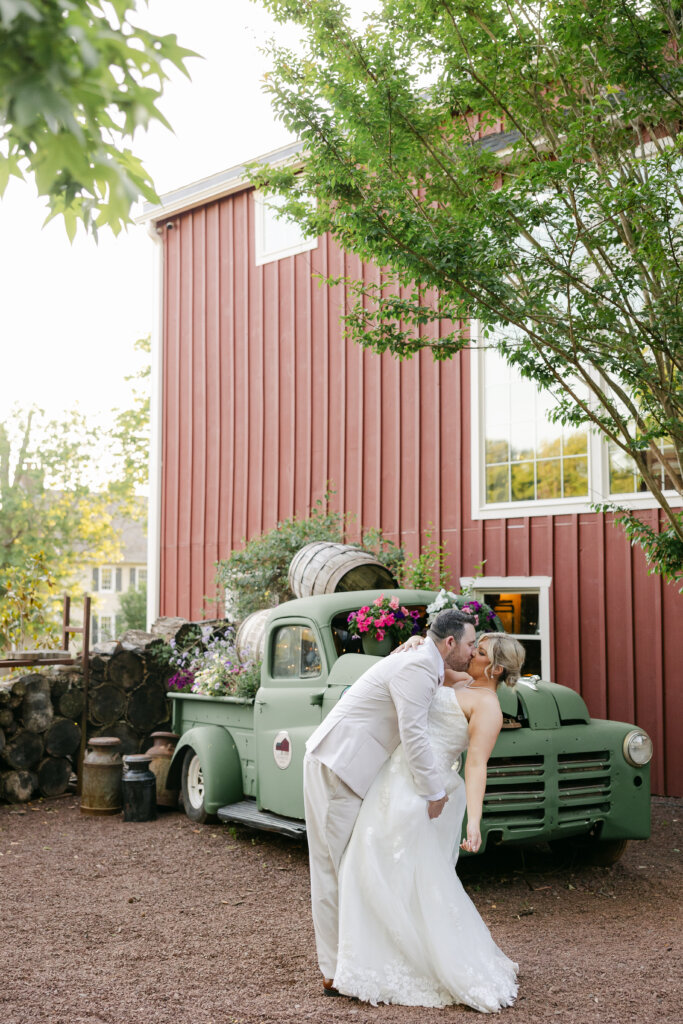 Bride and groom kissing in front of green truck at barn venue Lochwood Manor in Skippack PA