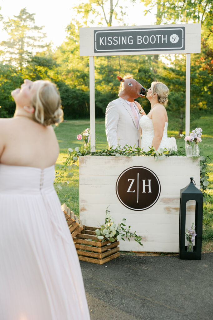 Bride and groom kissing at a kissing booth at Lochwood Manor. Groom wearing funny mask