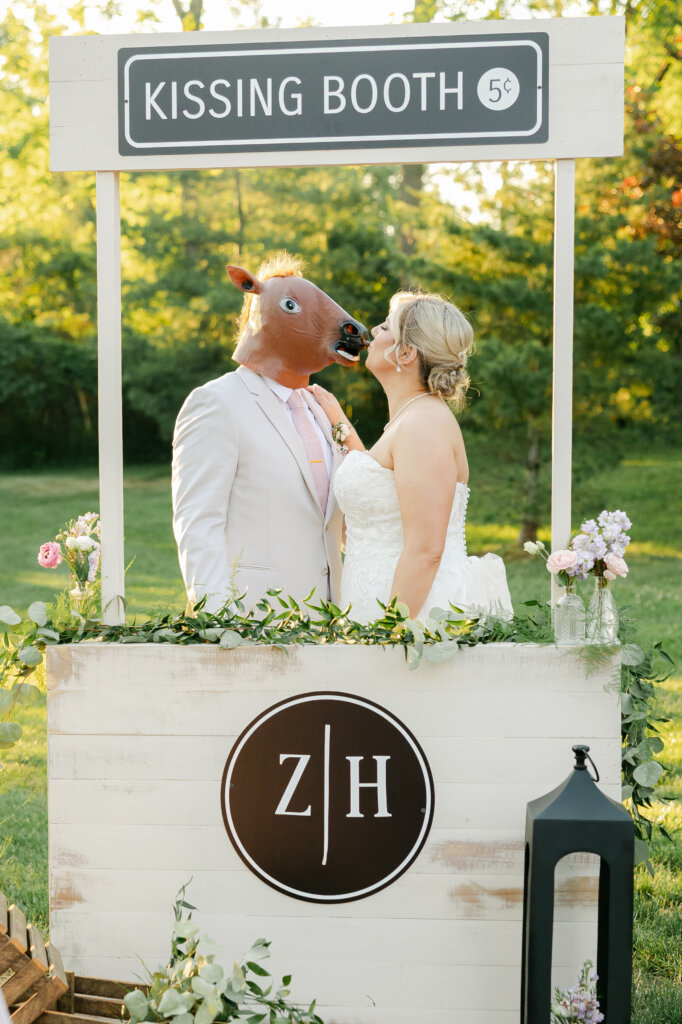 Bride and groom kissing at a kissing booth at Lochwood Manor. Groom wearing funny mask